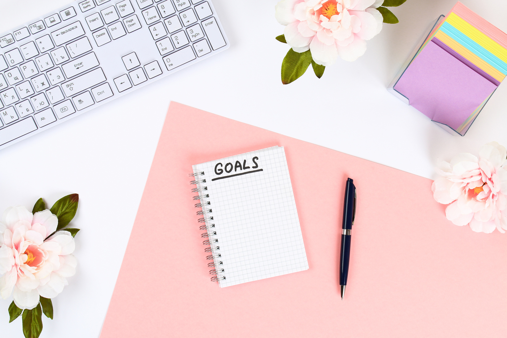 Write a Goal for the New Year 2010 in a White Notebook on a White Desktop Next to a Coffee Mug and a Keyboard. Top View, Flat Layout.